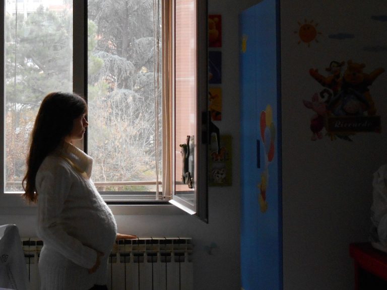 donna in gravidanza pensierosa guarda dalla finestra, in cerca di ispirazione per il nome della bambina